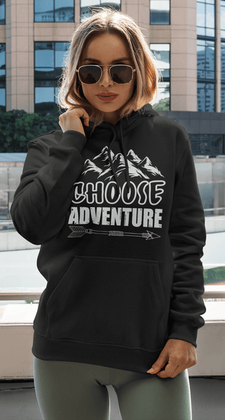Female standing with building in background wearing black hoodie with "Choose Adventure" design on the front, Available from the Xpert Apparel Store.