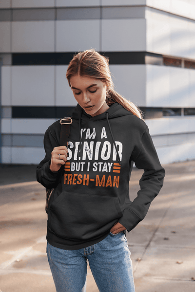 Girl standing at bus stop with backpack  wearing black Hoodie with I'm a Senior But I Stay Fresh-man T-shirt design from the Xpert Apparel Store