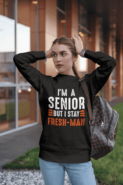 Girl standing outside fixing her hair wearing black sweatshirt with I'm a Senior But I Stay Fresh-man T-shirt design